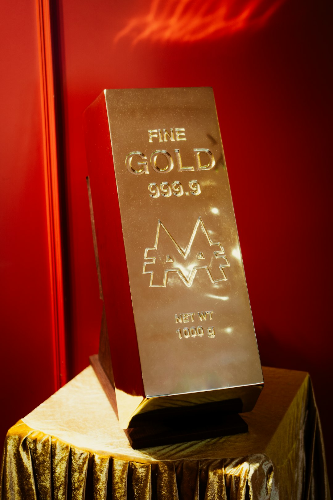 A massive, gleaming gold bar prop stands as a monument to wealth at a Monopoly exhibition. Engraved with FINE GOLD 999.9 and the iconic M logo, the bar sits on a gold-draped pedestal.